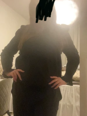 Svart blus med volangdetaljer - Säljer en svart blus med långa ärmar och snygga volangdetaljer på axlarna. Blusen har en lös passform och är perfekt för dig som gillar en stilren men ändå trendig look. Materialet känns mjukt och bekvämt mot huden. Lite V ringad vid bröstet