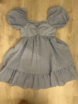 Blårutig kort klänning med puffärm - Supersöt kort klänning i blåvitt rutigt mönster med puffiga kortärmar och volangkant nertill. 