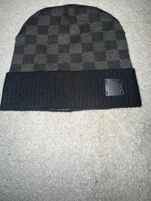 Lyxig monogrammössa i svart/grå – stilren & varm - Snygg stickad mössa i svart och mörkgrått med diskret monogrammönster över hela mössan. Klassisk modell med uppvikt kant och stilren läderpatch framtill. Invändigt finns broderad logotypetikett. Perfekt för höst och vinter – både varm och trendig, passar lika bra till vardags som till en mer uppklädd look. Mjuk och skön kvalitet med stretch som sitter bra på huvudet. Skicka gärna meddelande vid frågor eller om du vill ha fler bilder!🤗