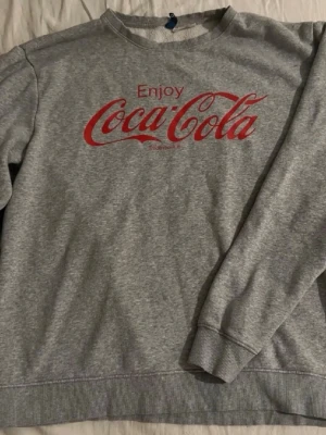 Sweatshirt - Säljer en grå sweatshirt med Coca-Cola-tryck på bröstet. I bra skick!