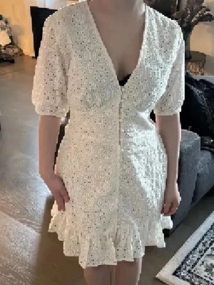 Vit spetsklänning med volang - Superfin vit kort Adoore liknade klänning med broderade hålmönster, v-ringning och knappar framtill. Puffiga korta ärmar och volangkant nertill ger en romantisk vibe. Perfekt för sommarens alla tillfällen! Superfin till sommaren. Helt ny med lappar köpt 699
