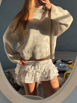 Beige ribbstickad polotröja - Säljer en oversized, ribbstickad polotröja i beige med breda ärmar och hög krage. Tröjan har en avslappnad passform och är perfekt för lager-på-lager-stil. Materialet ser mjukt och mysigt ut, perfekt för kyligare dagar.