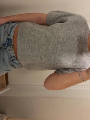 Grå stickad topp - Snygg grå stickad topp från Gina med korta ärmar och rund hals. Perfekt till ett par jeans för en chill och trendig look. Enkel och stilren design som passar till många outfits. I storlek 170 men sitter som XS/S. Inte nopprig eller stickig. 