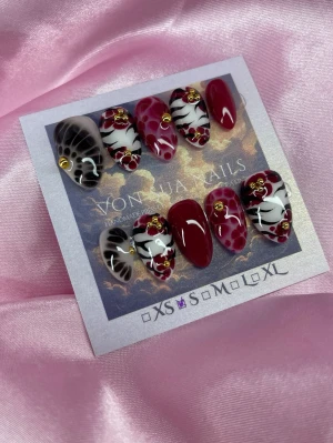 CherrySafari (S);Short Almond - Snygga handgjorda press-on naglar i en kort mandelform. Mix av vinröda, zebramönstrade och svarta naglar med detaljer i guld och små röda hjärtan. Handgjorda och dekorerade för en unik look. Perfekt för dig som vill sticka ut med coola och trendiga naglar.S: 15 mm, 11,5 mm, 12 mm, 11 mm, 9 mm 