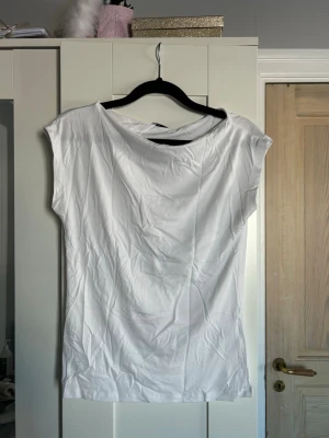 Vit ärmlös topp  - En basic vit topp från 157 med enkel och clean design. Toppen är ärmlös och har en rund halsringning. Perfekt att styla till jeans eller kjol för en fräsch look. Tillverkad i mjuk bomull som känns skön mot huden. Aldrig använd så i väldigt bra skick! Prislappen är kvar