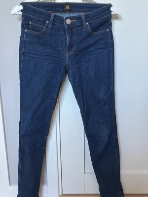 Mörkblå skinny jeans från Lee W26L31 - Snygga mörkblå skinny jeans från Lee med klassisk femficksmodell och orange kontrastsömmar. Jeansen har normal midja och är tillverkade i ett stretchigt denimtyg för skön passform. Perfekta till en avslappnad streetstyle-look.
