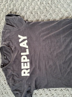 Svart t-shirt från Replay - Cool svart t-shirt från Replay med stort vitt tryck på bröstet. Klassisk rund halsringning och korta ärmar. Tillverkad i mjuk bomull som känns skön mot huden. Perfekt för en avslappnad och trendig look.