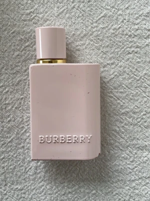 Burberry Her Eau de Parfum 30ml - Upplever ca.50-60% kvar i flaskan. Den har en skada på botten men flaskan är hel i sig. Se sista bilden med markering för nivån av innehållet 😇 Burberry Her Eau de Parfum i en stilren, ljusrosa rektangulär flaska med guldiga detaljer. Flaskan har en modern design med Burberry-loggan i relief. Perfekt för dig som gillar eleganta och trendiga dofter. 