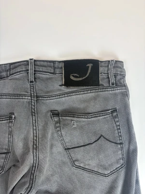 Gråa slim fit jeans från Jacob Cohen - Snygga gråa slim fit jeans från Jacob Cohen med klassisk femficksmodell och svart patch med J-logga bak. Jeansen har raka ben och är tillverkade i mjuk denim med diskreta slitningar. Perfekta för en avslappnad men stilren look.