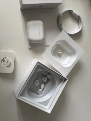 Apple AirPods Pro med laddningsetui - Säljer ett par vita Apple AirPods Pro med trådlöst laddningsetui. Hörlurarna har silikontoppar i olika storlekar, brusreducering och levereras med originalkartong, laddningskabel och extra öronproppar. Perfekta för musik, samtal och träning.