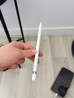 Apple Pencil med rosa fodral - Säljer en Apple Pencil i vit färg med slimmad design och metallisk detalj vid toppen. Medföljer ett skyddande fodral i vitt och rosa som har plats för tillbehör. Perfekt för dig som vill rita eller anteckna digitalt på din iPad.