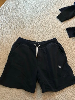 Mörkblåa shorts från U.S. POLO ASSN. - Mörkblåa shorts från U.S. POLO ASSN. med vit snörning i midjan och broderad logga på ena benet. Mjukt material och två sidofickor gör dem både snygga och bekväma. Perfekta för sommaren eller chill dagar. Det står att byxorna är storlek L men kolla inte på det!!! Passar storlek S och M de är konstiga i storleken.
