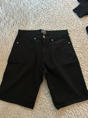 Svarta slim fit shorts från H&M - Snygga svarta shorts från H&M i slim fit-modell. Klassisk fyrficksdesign med knapp och dragkedja framtill. Perfekta för dig som gillar en stilren och enkel look. Det är fin material. Storlek 29 knappast använda