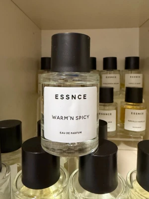 ESSNCE Warm'n Spicy Eau de Parfum - ESSNCE Warm'n Spicy Eau de Parfum kommer i en rund, genomskinlig glasflaska med svart lock och stilren vit etikett. Doften har en varm och kryddig karaktär, perfekt för dig som gillar unika och intensiva parfymer.