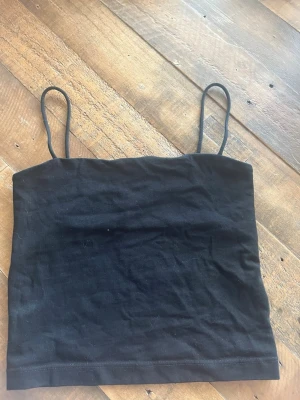 Svart linnetopp från Gina Tricot - En svart, enkel linnetopp från Gina Tricot med tunna axelband. Toppen är rak i modellen och tillverkad i mjuk bomull, perfekt att styla med jeans eller kjol. Snygg och basic för en clean look.