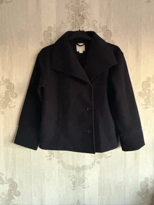 Kappa från Gina Tricot - Stilren  kappa från Gina Tricot med bred krage och tre knappar framtill. Kortare modell som passar perfekt till höstens och vinterns outfits. Klassisk design som är lätt att matcha med olika stilar.