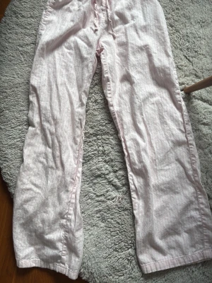 Ljusrosa pyjamasbyxor från Gina Tricot - Mysiga ljusrosa pyjamasbyxor från Gina Tricot med diskreta vita ränder. Byxorna har resår i midjan för extra komfort och är tillverkade i ett mjukt bomullsmaterial. Perfekta för chillkvällar hemma.