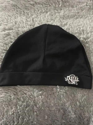 Svart mössa från Sztiah - Svart mössa i mjukt tyg från Sztiah med vit broderad logga framtill. Enkel och stilren design som passar perfekt till streetwear och vardagsoutfits. Mössan har en klassisk passform och är lätt att matcha med olika stilar.