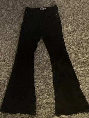 Svarta utsvängda jeans - Snygga svarta jeans med utsvängda ben och klassisk femficksdesign. Perfekta för dig som gillar en retrostil med modern twist. Jeansen har hög midja och är tillverkade i ett stretchigt denimtyg för extra komfort. Är i short modell. 