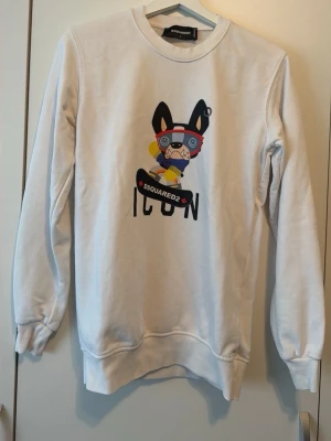 Vit sweatshirt ICON - Vit sweatshirt från med tryck av en tecknad hund med glasögon och skateboard. Tröjan har rund hals, långa ärmar och ribbade muddar. Materialet är mjukt och bekvämt, säljer eftersom den inte kommer till användning
