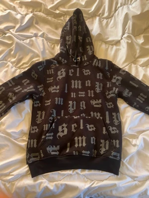 Svart hoodie Palm Angels - Säljer en svart hoodie med stor huva och gotisk text i grått över hela plagget. Hoodien har en stor magficka och ribbade muddar vid ärmar och nederkant. Perfekt för dig som gillar streetwear och vill sticka ut med en unik design.