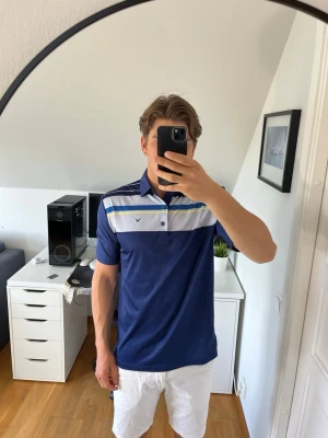 Blå randig piké från Callaway - Snygg blå pikétröja från Callaway med vita, gråa och gula ränder över bröstet. Klassisk krage och knappar framtill. Tillverkad i mjukt och svalt material. Hör gärna av dig vid frågor!