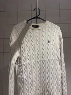 Morris tröja - Vit kabelstickad tröja från morrris med rund halsringning och broderad logotyp på bröstet. Tröjan har långa ärmar och ribbade muddar vid ärmslut och nederkant. 