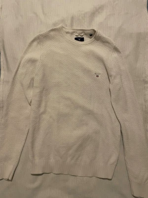 Vit stickad tröja från Gant - Vit stickad tröja från Gant med diskret strukturmönster och broderad logga på bröstet. 
