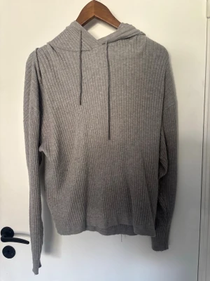 Grå ribbad hoodie från 157 - Mysig grå hoodie från 157 i ribbstickat material. Hoodien har dragsko i huvan och långa ärmar. Perfekt för dig som gillar en enkel och stilren look med lite extra struktur tack vare ribbningen.