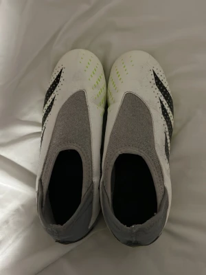 Adidas Predator vita fotbollsskor - Säljer ett par Adidas Predator fotbollsskor i vitt med svarta och neongula detaljer. Skorna har en strumpliknande grå ovandel och mönstrad sula för bra grepp på planen. Perfekta för dig som vill ha kontroll och stil på fotbollsplanen. Pris kan diskuteras !