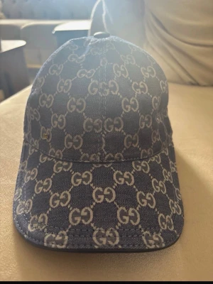 Blå GG-mönstrad keps  - Snygg blå keps . Kepsen är tillverkad i denimliknande material och har justerbar rem baktill. Insidan är fodrad i ljus textil och har märkets etikett. Perfekt för en trendig streetstyle-look.