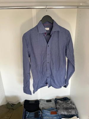 Blå skjorta från Eton med röda detaljer - Snygg blå skjorta från Eton i contemporary fit. Skjortan har diskret rutigt mönster och röda detaljer på insidan av kragen. Hör gärna av dig vid frågor! 
