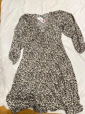 Leopardmönstrad klänning från Thernlunds (Dry Lake) - Säljer en snygg leopardmönstrad klänning från Thernlunds (Dry Lake) med v-ringning och knappar framtill. Klänningen har trekvartsärm och är i en ljus ton med svarta och bruna detaljer. Perfekt för dig som vill sticka ut lite extra.