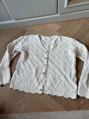 Vit stickad kofta med mönster - Snygg vit stickad kofta med v-ringning och dekorativa knappar framtill. Koftan har ett fint diamantmönster och vågig nederkant. Långärmad och tillverkad i mjukt material, perfekt att slänga på sig. Koftan saknar en knapp (bild 3) men märks inte så mycket. Prislappen är inte kvar men koftan är köpt utomlands. Skriv för fler bilder. Pris går att diskutera!❤️