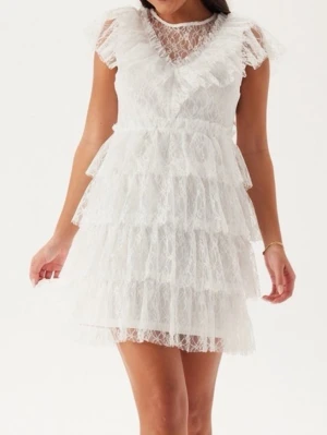 Student klänning  - Lace Frill Short Dress BUBBLEROOM OCCASION, enbart testad storlek xs Supersöt vit kortklänning i spets med flera lager volanger och v-ringning. Klänningen har genombrutna spetsdetaljer, korta ärmar och en feminin siluett. Perfekt för dig som vill ha en romantisk och trendig look.