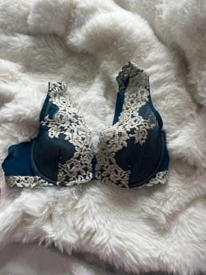 Intimissimi bh - Snygg mörkgrön bh med vacker vit spets och blommiga detaljer. Bh:n har bygel och justerbara axelband. Materialet är en mix av satin och spets som ger en lyxig känsla. Perfekt för dig som gillar feminina och eleganta underkläder.