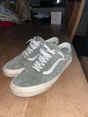 Gråa Vans Old Skool sneakers - Snygga Vans Old Skool sneakers i grå mocka med vita detaljer och klassisk vit sula. Skorna har den ikoniska sidoremsan och vita skosnören. Perfekta för en avslappnad streetstil.
