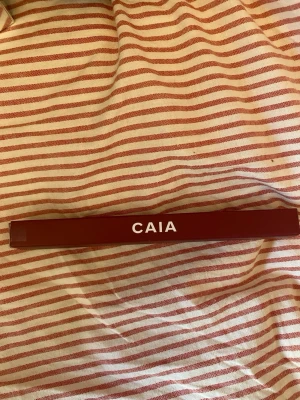 CAIA Ruby Plum läppenna - Öppnad och testad på handen!! Snygg läppenna från CAIA i färgen Ruby Plum. Pennan har en djup plommonröd nyans och kommer i en smal, klassisk form. Perfekt för att definiera läpparna och skapa en markerad look. Förpackningen är stilren i matchande färg med vit text.