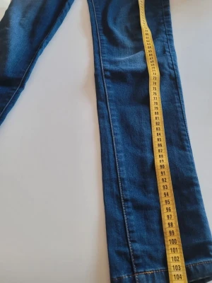 DESIGUAL Blå skinny jeans med hjärta.i - Säljer ett par blå skinny jeans med snygga detaljer som broderi vid fickan och ett litet rött hjärta. Klassisk femficksmodell med dragkedja och knapp. Jeansen har smal passform och är tillverkade i mycket stretchigt denimtyg för extra komfort och är Supersköna.