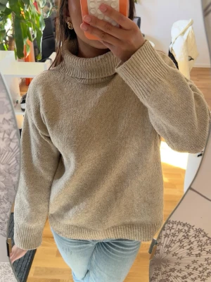 Beige stickad polotröja - Mysig beige stickad polotröja med bred krage och långa ärmar. Tröjan har en avslappnad passform och ribbstickade muddar vid ärmslut och nederkant. Perfekt för lager-på-lager och enkel att matcha med jeans eller kjol.