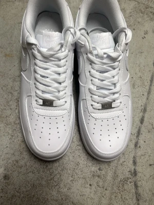 Nike Air Force 1 vita sneakers - Klassiska helvita Nike Air Force 1 sneakers i läder med perforerad tå, vit sula och ikonisk Swoosh på sidorna. Skorna har låga skaft och vita skosnören. Perfekta för en clean och stilren look. Inga tecken på slitage, kan absolut tänka mig gå ner i pris. Storlek 40,5 men stor i sulan (25,5cm). Har du frågor tveka inte på att skicka 🤙🏼 Jag kan absolut tänka mig gå ner i pris! 
