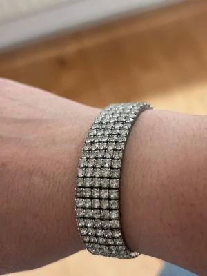 armband med glittrande pärlor - Snyggt och brett armband med flera rader glittrande, klara pärlor i silverfärgad infattning. Armbandet har en flexibel design som sitter bekvämt runt handleden och ger en riktigt lyxig känsla. Perfekt för dig som gillar att sticka ut med accessoarer.