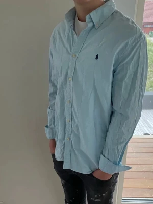 Ljusblå skjorta från Ralph Lauren - Klassisk ljusblå skjorta från Ralph Lauren. Skjortan har långa ärmar och knäppning framtill. Perfekt för våren och sommaren 