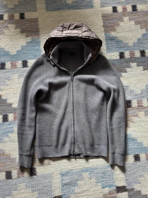 massimo dutti cardigan - Säljer en grå stickad hoodie från Massimo Dutti med hel dragkedja framtill och avtagbar quiltad huva i beige. Tröjans tvättlapp är avkilpt, Tröjan har ribbstickad struktur och långa ärmar. Perfekt för dig som gillar stilren och modern design. Lite nopprig :)