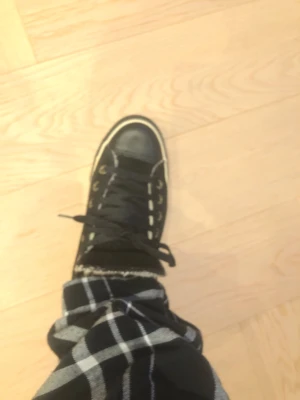 Svarta Converse All Star high tops - Klassiska svarta Converse All Star high tops med vita detaljer och snörning. Skorna har vit sula och tå, samt All Star-logga baktill. Tillverkade i canvas med gummisula, perfekta för en avslappnad och cool stil.