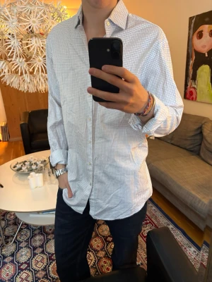 Vit rutig skjorta  - Klassisk vit skjorta med diskret rutmönster. Skjortan har lång ärm, knappar framtill och en avslappnad passform. 