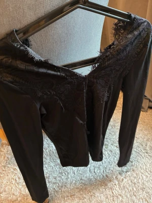 Svart långärmad topp med spets - Snygg svart långärmad topp med v-ringning och dekorativ spetsdetalj över axlar och urringning. Toppen har en figurnära passform och är perfekt för dig som gillar stilrena plagg med en twist. Materialet känns mjukt och stretchigt. Aldrig använd och normal i storleken. Nypris ca 450kr