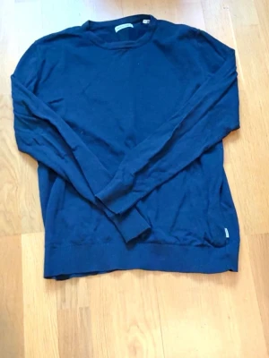 Mörkblå basic tröja - En enkel och stilren mörkblå tröja med rund halsringning och långa ärmar. Tröjan har ribbade muddar vid ärmslut och nederkant, perfekt för en clean och avslappnad look. Materialet ser ut att vara mjukt och lätt, passar bra till jeans eller chinos.