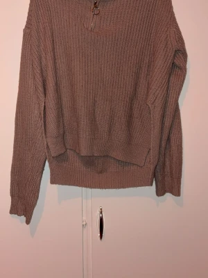 Brun/grå  stickad tröja med dragkedja - Mysig brun/grå  stickad tröja med hals dragkedja och ringdetalj vid halsen. Tröjan har lång ärm, ribbstickade muddar och en avslappnad passform. Perfekt för lager på lager och enkel att styla till olika outfits.