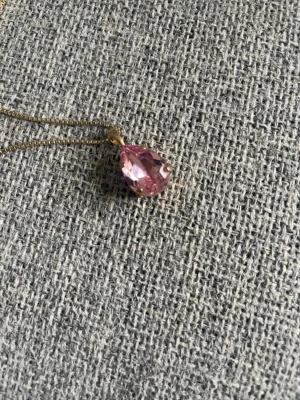 Caroline Svedbom halsband rosa droppformad sten - Snyggt halsband med en droppformad, rosa glittrande sten i facetterad design. Kedjan är tunn och guldfärgad vilket ger en elegant kontrast till stenen. Perfekt för dig som gillar stilrena och trendiga accessoarer.